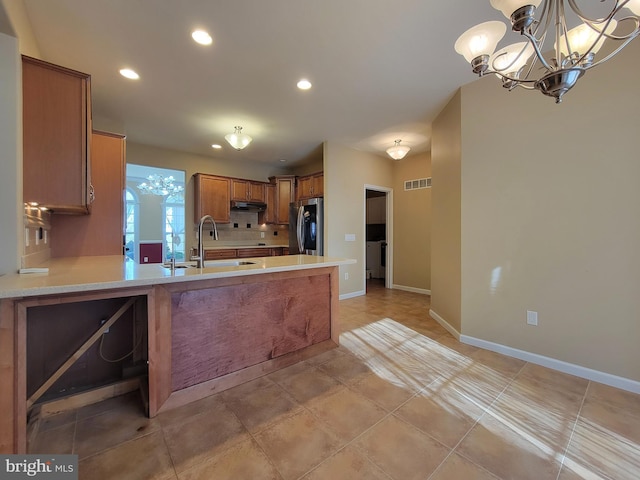 kitchen with kitchen peninsula, stainless steel refrigerator with ice dispenser, a notable chandelier, and sink