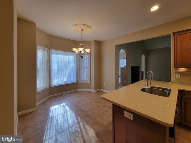 kitchen with kitchen peninsula, decorative light fixtures, an inviting chandelier, and sink