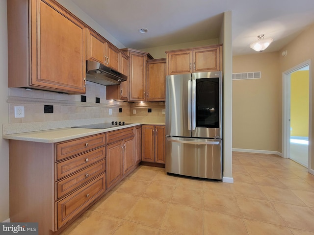 kitchen featuring black electric stovetop, stainless steel fridge, light tile patterned floors, and backsplash