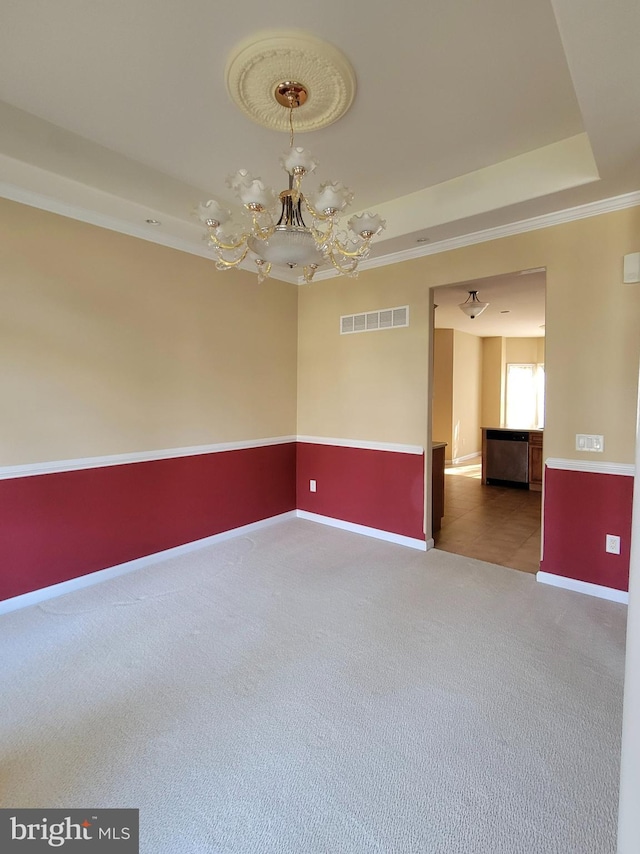 carpeted spare room featuring a tray ceiling and a notable chandelier