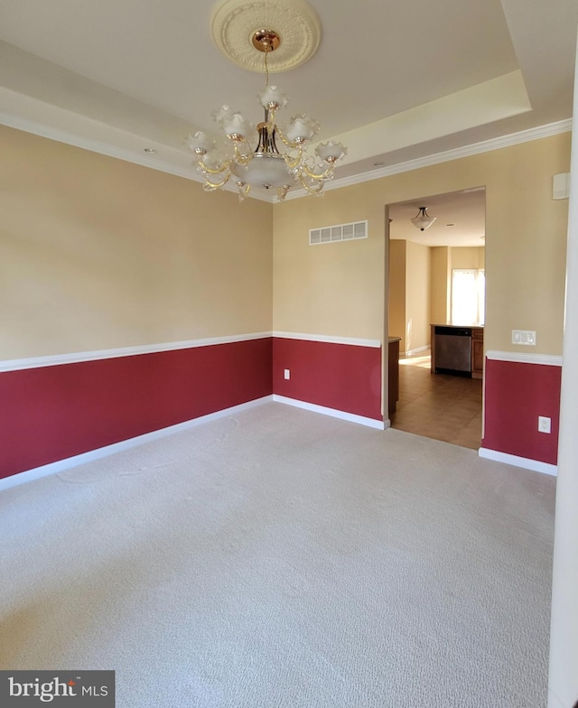 empty room featuring a raised ceiling, carpet, a chandelier, and ornamental molding