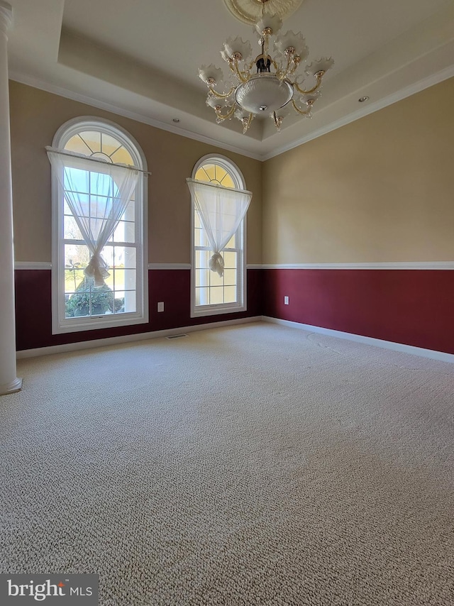 carpeted empty room featuring a raised ceiling, a notable chandelier, and crown molding