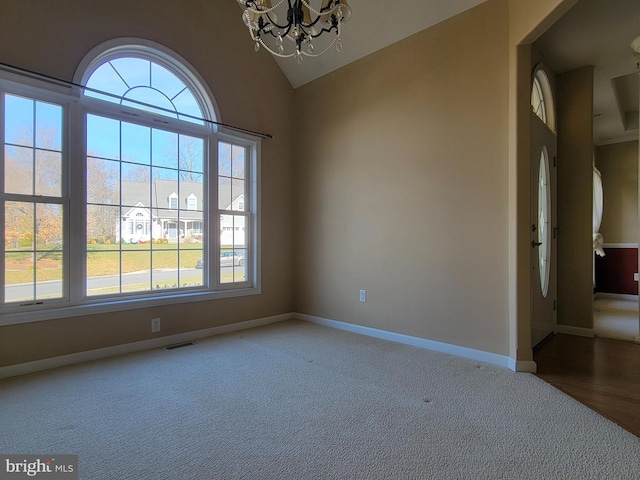 carpeted spare room with plenty of natural light, lofted ceiling, and a notable chandelier