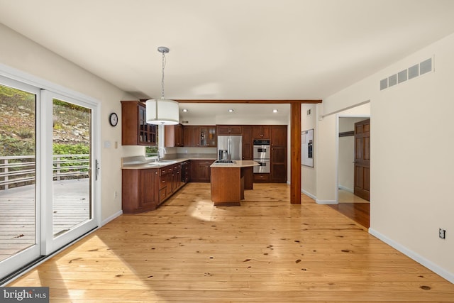 kitchen featuring a kitchen island, stainless steel appliances, sink, hanging light fixtures, and light hardwood / wood-style flooring