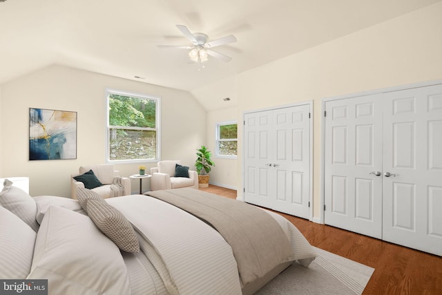 bedroom with lofted ceiling, ceiling fan, hardwood / wood-style floors, and two closets