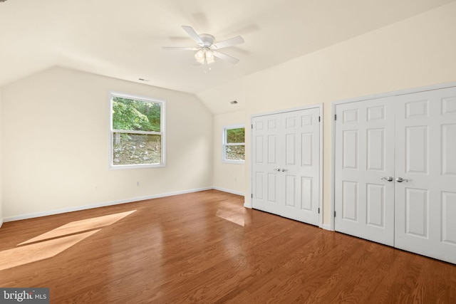 unfurnished bedroom featuring lofted ceiling, two closets, hardwood / wood-style floors, and ceiling fan