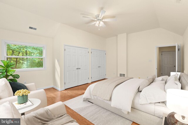 bedroom with ceiling fan, multiple closets, light hardwood / wood-style flooring, and vaulted ceiling