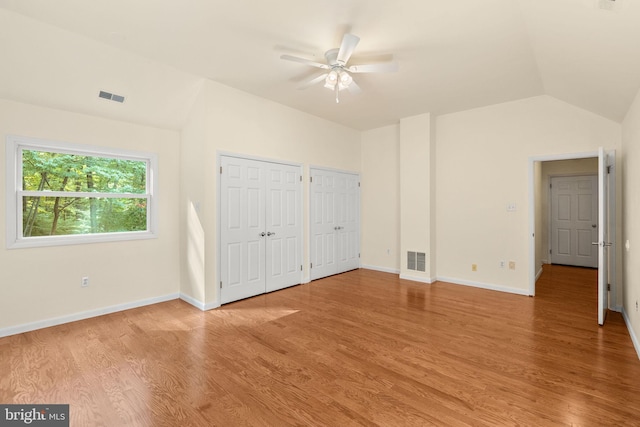 unfurnished bedroom with ceiling fan, multiple closets, hardwood / wood-style flooring, and vaulted ceiling