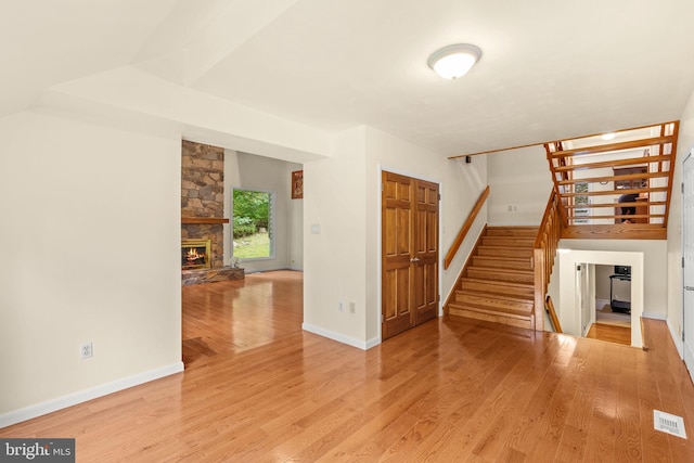 unfurnished living room with a stone fireplace and light wood-type flooring