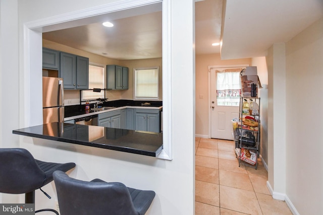 kitchen featuring light tile patterned flooring, sink, kitchen peninsula, stainless steel appliances, and a kitchen bar