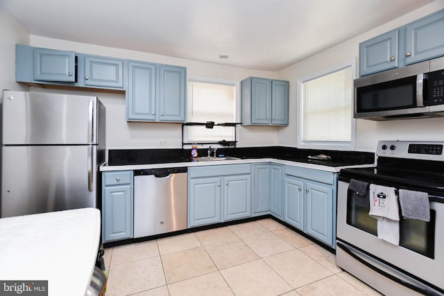 kitchen with blue cabinetry, appliances with stainless steel finishes, light tile patterned floors, and sink