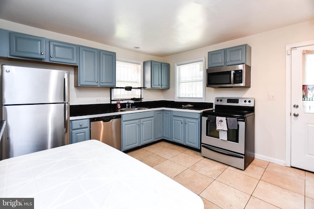 kitchen with blue cabinets, light tile patterned flooring, sink, appliances with stainless steel finishes, and tile counters