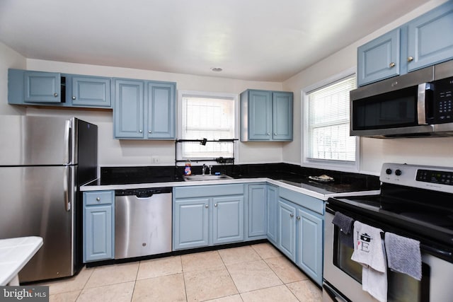 kitchen featuring blue cabinets, light tile patterned floors, stainless steel appliances, and sink