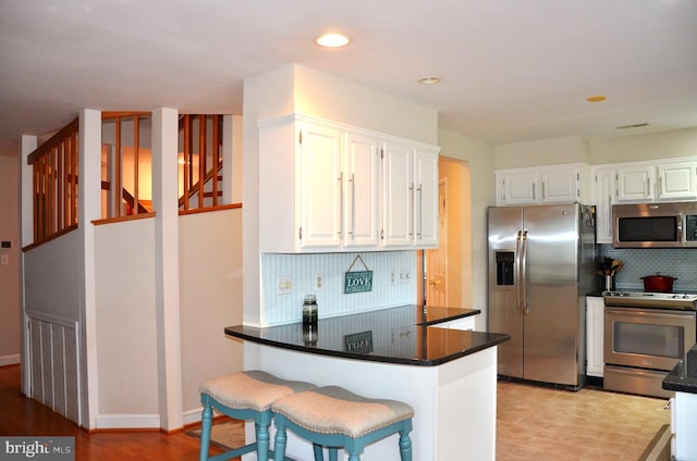 kitchen featuring white cabinetry, kitchen peninsula, appliances with stainless steel finishes, and tasteful backsplash