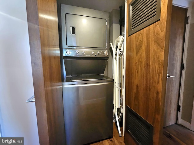 laundry area with laundry area, visible vents, stacked washer / dryer, and wood finished floors