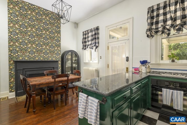 kitchen with dark wood-type flooring, a fireplace, green cabinetry, black oven, and radiator