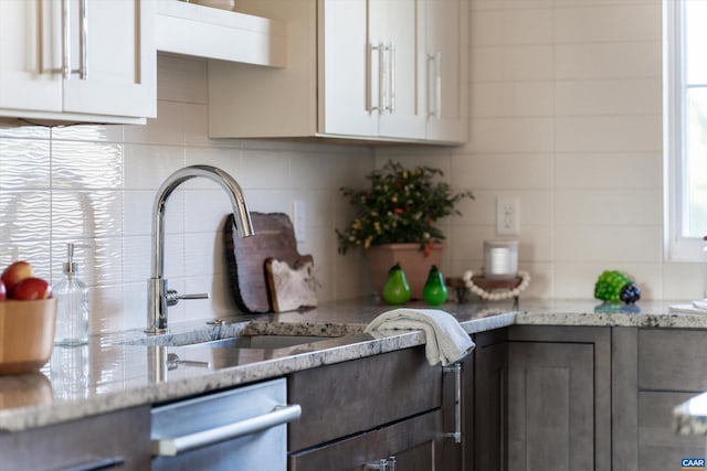 kitchen featuring light stone countertops, sink, white cabinetry, and stainless steel dishwasher