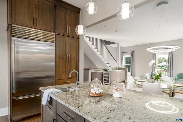 kitchen with stainless steel built in fridge, pendant lighting, wine cooler, wood-type flooring, and light stone countertops