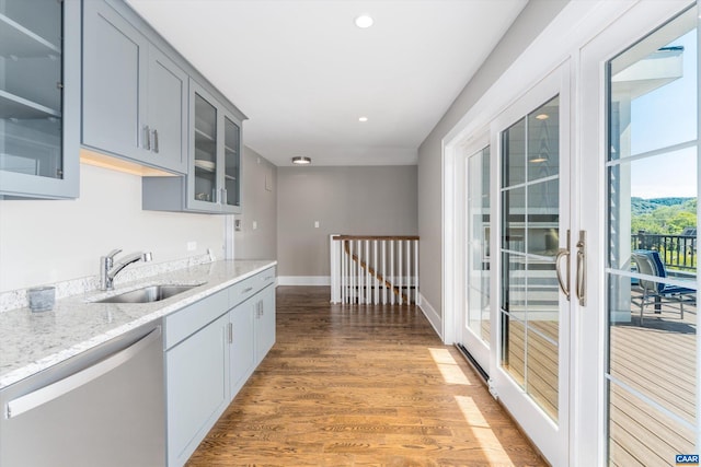 kitchen featuring dishwasher, light stone counters, hardwood / wood-style flooring, sink, and gray cabinetry