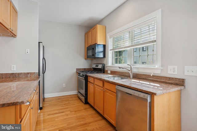 kitchen with light hardwood / wood-style floors, appliances with stainless steel finishes, sink, and light stone countertops