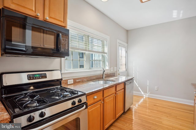 kitchen featuring light stone countertops, stainless steel appliances, light wood-type flooring, and sink