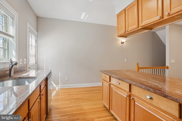 kitchen with light hardwood / wood-style flooring, light stone counters, stainless steel dishwasher, and sink