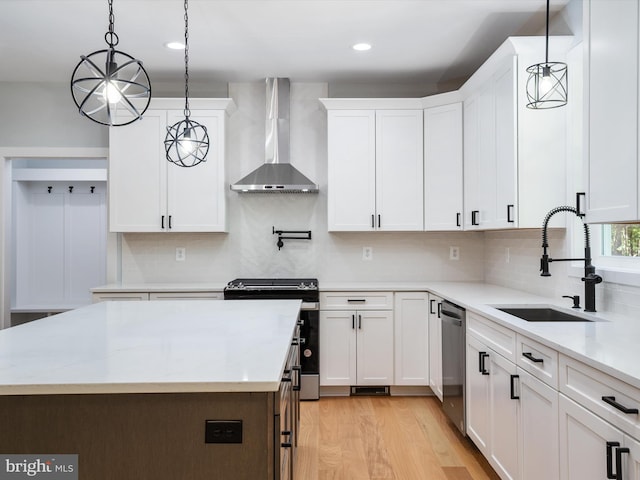 kitchen featuring wall chimney exhaust hood, sink, white cabinets, pendant lighting, and appliances with stainless steel finishes