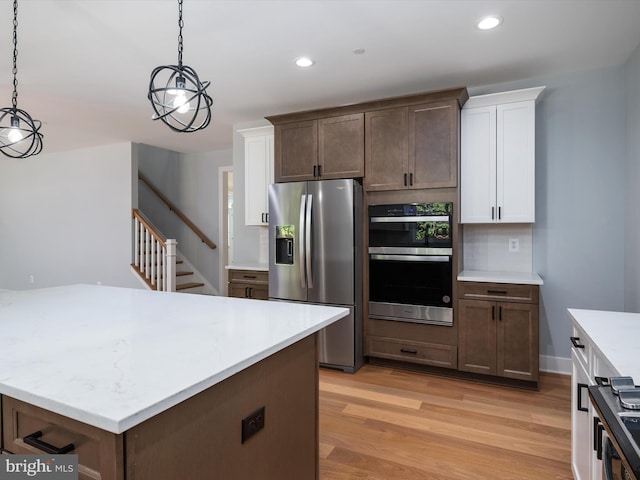 kitchen with appliances with stainless steel finishes, hanging light fixtures, light hardwood / wood-style flooring, and white cabinetry