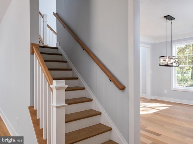 staircase featuring crown molding, hardwood / wood-style flooring, and a chandelier