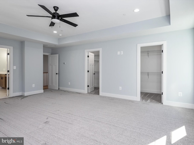 unfurnished bedroom featuring a walk in closet, ensuite bathroom, light colored carpet, and ceiling fan