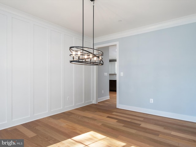 unfurnished dining area featuring a notable chandelier, ornamental molding, and hardwood / wood-style floors