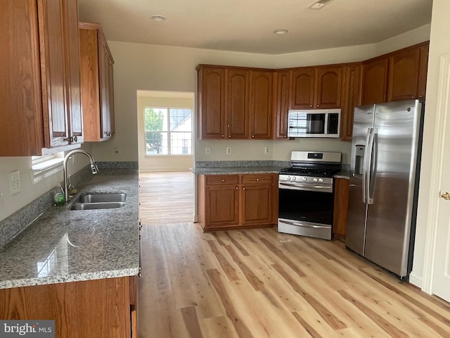 kitchen with appliances with stainless steel finishes, light wood-type flooring, sink, and stone countertops