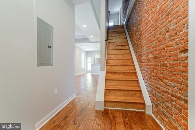 stairs featuring brick wall, electric panel, and hardwood / wood-style floors