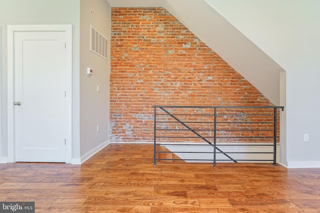 additional living space featuring wood-type flooring and brick wall