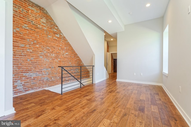 bonus room with hardwood / wood-style floors and brick wall