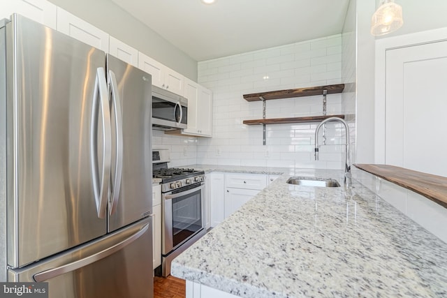 kitchen with sink, white cabinetry, stainless steel appliances, light stone countertops, and decorative backsplash