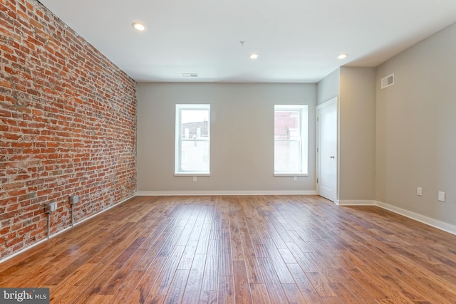 unfurnished room featuring hardwood / wood-style floors, brick wall, and a healthy amount of sunlight