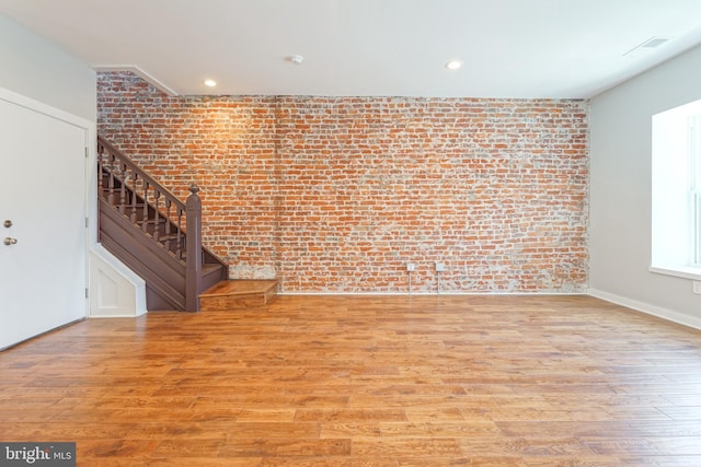 unfurnished living room with light wood-type flooring and brick wall