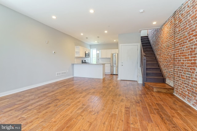 unfurnished living room featuring light hardwood / wood-style flooring and brick wall