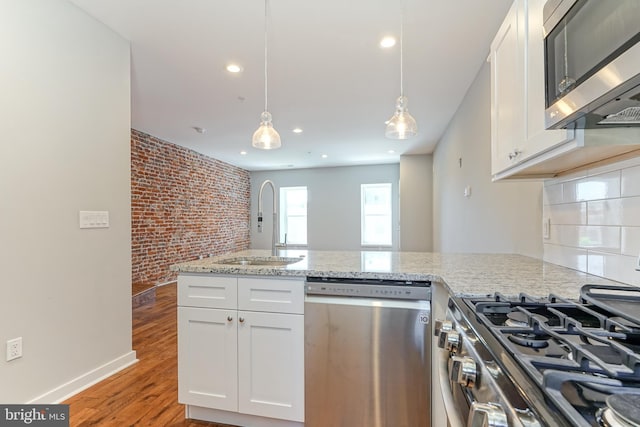 kitchen with light stone counters, white cabinets, pendant lighting, stainless steel appliances, and light hardwood / wood-style flooring