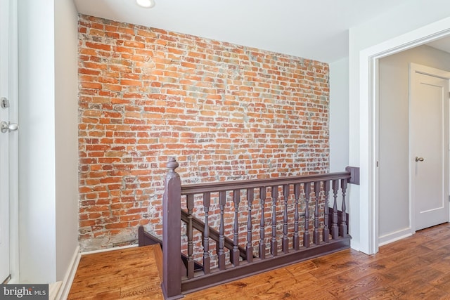 staircase with brick wall and hardwood / wood-style flooring