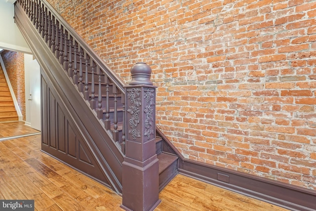 staircase featuring brick wall and hardwood / wood-style floors