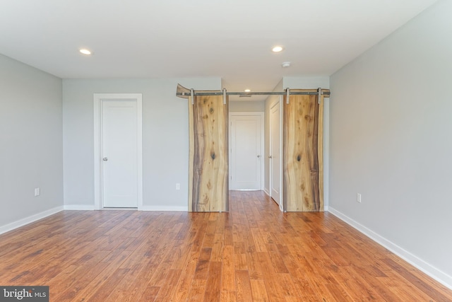 unfurnished bedroom with a barn door and light hardwood / wood-style floors