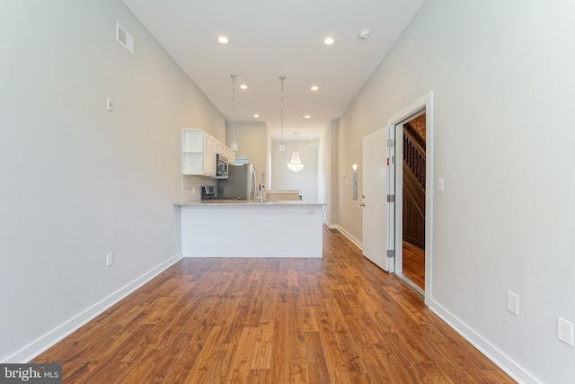 kitchen featuring hanging light fixtures, kitchen peninsula, hardwood / wood-style floors, and white cabinets