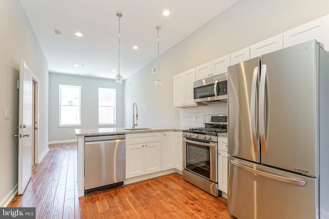 kitchen with light stone counters, light hardwood / wood-style floors, white cabinets, hanging light fixtures, and stainless steel appliances