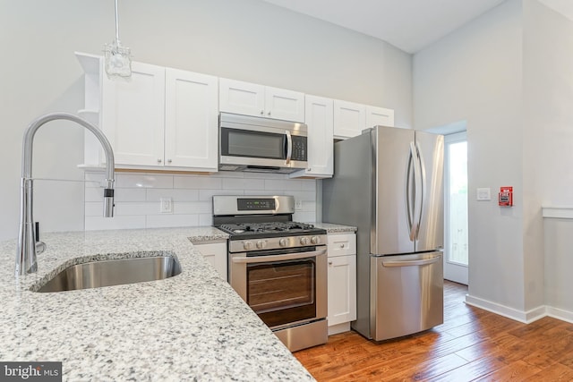 kitchen with appliances with stainless steel finishes, white cabinetry, light stone countertops, wood-type flooring, and sink