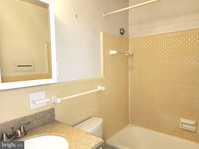 full bathroom with tile walls, vanity, tiled shower / bath, and toilet