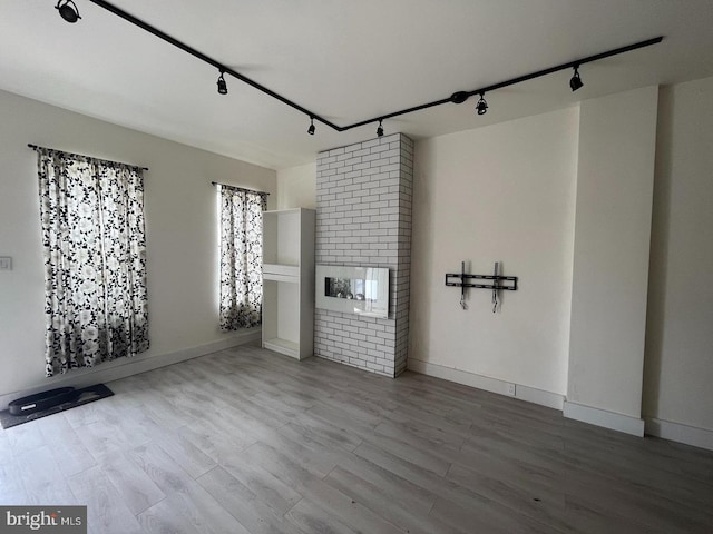 unfurnished living room with a brick fireplace, hardwood / wood-style flooring, and track lighting