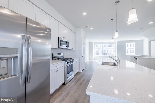 kitchen with appliances with stainless steel finishes, white cabinets, pendant lighting, light hardwood / wood-style flooring, and sink