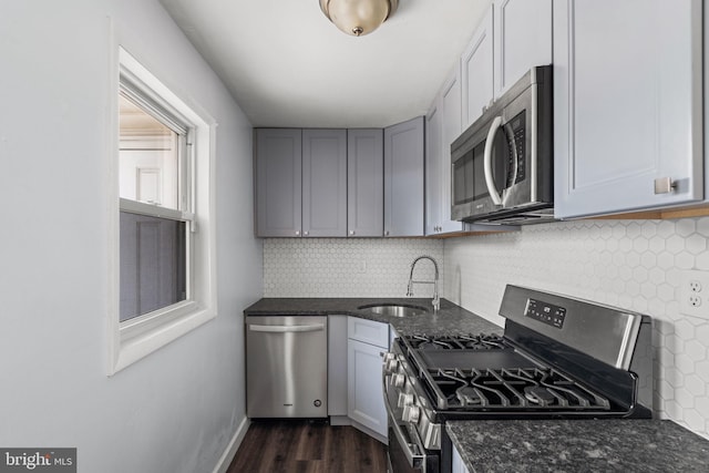 kitchen with sink, tasteful backsplash, dark wood-type flooring, appliances with stainless steel finishes, and dark stone countertops